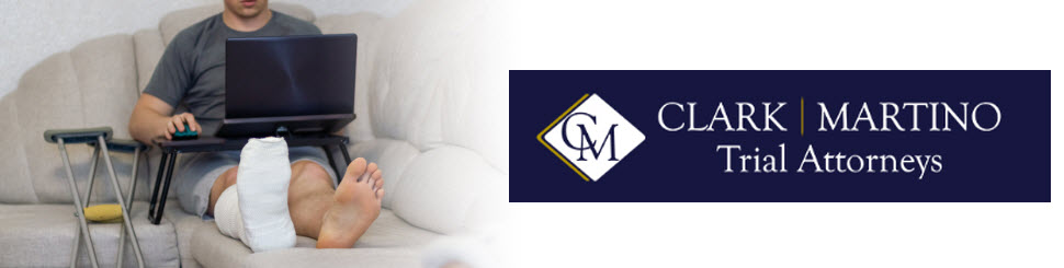 A man sits on a sofa in a cast with a laptop